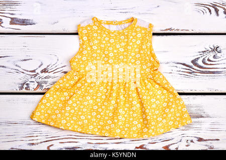 Baby-ragazza carina giallo abito di cotone. toddler girl sleeveless modellato sul top bianco sullo sfondo di legno. Foto Stock