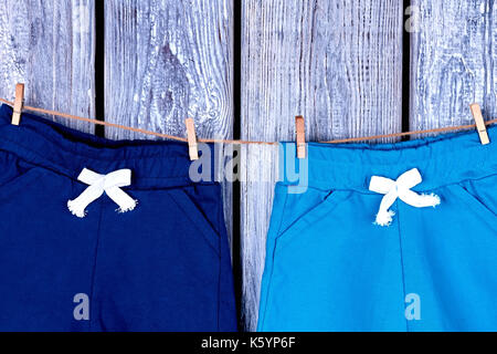 Bambini pantaloni appesi sulla fune. bambini shorts in cotone essiccazione su stendibiancheria sul vecchio sfondo di legno. Foto Stock