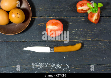 Affettare i pomodori con un coltello da tasca. Sfondo scuro. Foto Stock