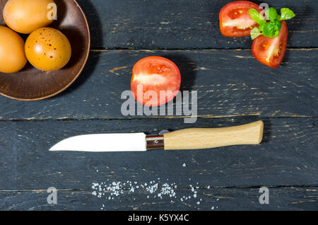 Affettare i pomodori con un coltello da tasca. Lay piatto. Sfondo scuro. Foto Stock