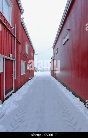 Tracce di pneumatici nella neve di vicolo stretto tra il rosso porta murata magazzini che conduce al ponte del molo in legno del porto costruito su palafitte. hamno Foto Stock