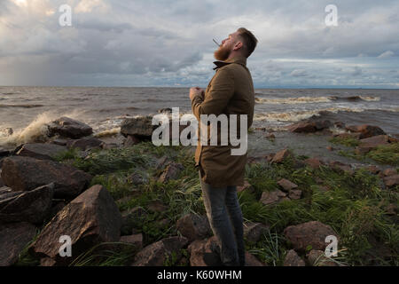 Uomo Barbuto con una sigaretta in riva al mare in tempesta meteo Foto Stock