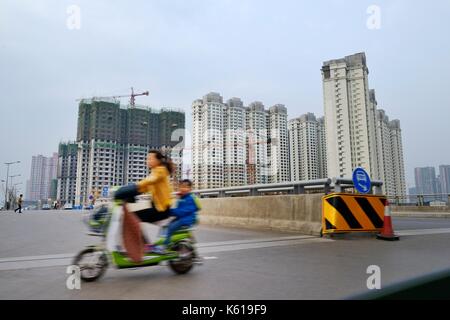 Città di Taiyuan, shanxi, Cina. donna e bambino sul ciclomotore passare alcune delle tante nuove e in costruzione blocchi di appartamenti Foto Stock