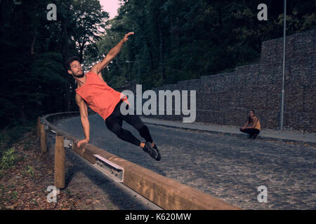 Due giovani, avventura, foresta di strada all'aperto, uomo jumping recinto parkour, street stunt, area rurale, donna sfondo dietro, il salto in aria Foto Stock