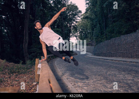 Due giovani, avventura, foresta di strada all'aperto, uomo jumping recinto parkour, street stunt, area rurale, salti in aria Foto Stock