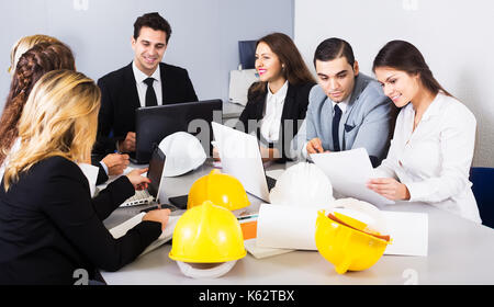 Il team di professionisti di positivo a discutere il progetto di business e sorridente in interni. concentrarsi sulla ragazza di destra Foto Stock