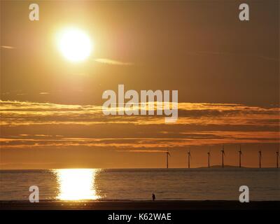 Camminare sulla spiaggia al tramonto con Robin Rigg dietro per centrali eoliche, maryport, cumbria, Regno Unito Foto Stock