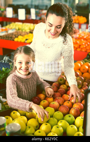 Ritratto di sorridenti madre e figlia piccola acquisto di mele mature al mercato. focus sulla ragazza Foto Stock