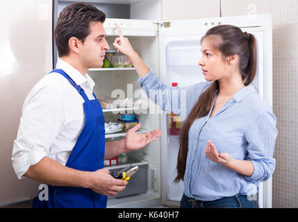 Preoccupato della donna che protestano tuttofare per problemi con il frigorifero in cucina Foto Stock