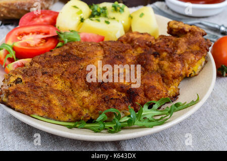 Golden schnitzel, patate bollite con insalata e pomodori su una piastra su un legno scuro dello sfondo. Foto Stock