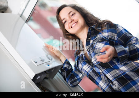 Ritratto di ordinaria sorridente ragazza utilizzando acqua di riscaldamento a casa Foto Stock