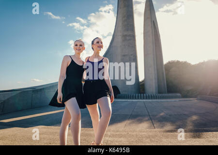 Due femmina ballerini in piedi insieme all'esterno. Balletto sorridente artisti che posano per una foto davanti a un monumento. Foto Stock