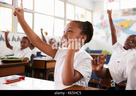 Schoolgirl alzando la mano durante una lezione a scuola elementare Foto Stock