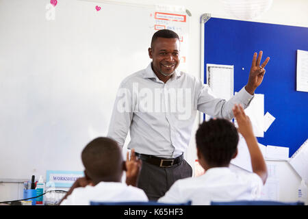 Insegnante che mostra la mano di fronte a una scuola elementare di classe Foto Stock