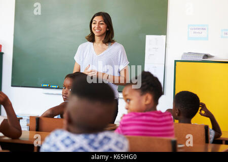 Femmina insegnante di volontariato nella parte anteriore della classe presso una scuola elementare Foto Stock