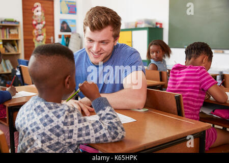 Maschio bianco aiutando insegnante di scuola elementare boy in classe Foto Stock