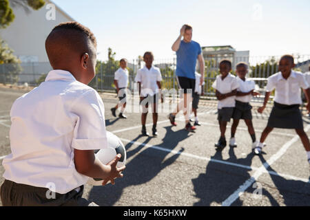 Insegnante gioca a calcio con i bambini nel parco giochi a scuola Foto Stock