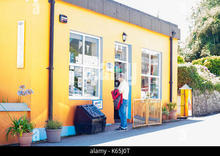 Uomo in piedi al di fuori di un negozio di giallo la lettura dei bandi di gara nella finestra di ricerca nella finestra su un luminoso estati soleggiate giorno, Kerry Irlanda Foto Stock