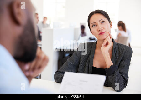 Il pensiero della donna durante un colloquio di lavoro in un ufficio open space Foto Stock