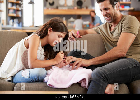 Figlia seduti sul divano di casa padre pittura le unghie Foto Stock