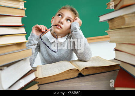 Trasognata School girl, guardando verso l'alto. foto della bambina con il libro aperto, fantasticando o pensando a qualcosa. Il concetto di istruzione Foto Stock