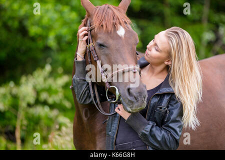 Giovane donna con il suo cavallo arabo in piedi nel campo Foto Stock