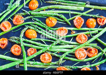 Arrosto di freschi Asparagi verdi lance e i pomodori ciliegia condito con rosmarino e sale su un vassoio da forno visto dal di sopra per un antipasto gourmet Foto Stock