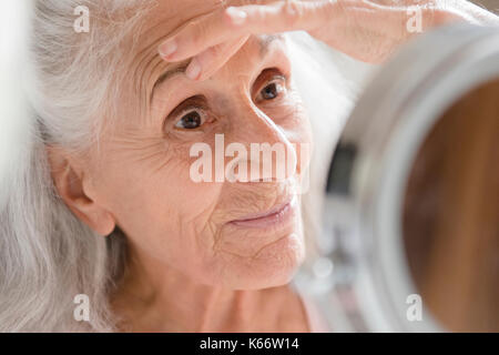 Donna anziana controllo occhio rughe in specchio Foto Stock