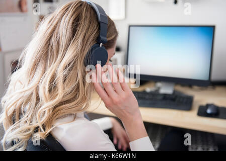 La donna caucasica ascoltando le cuffie al computer desk Foto Stock