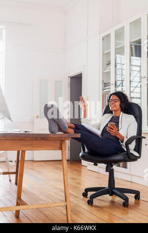 Razza mista donna con i piedi fino in ascolto per telefono cellulare con le cuffie Foto Stock