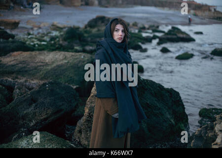 Caucasian donna che indossa foulard rocce vicino al mare Foto Stock