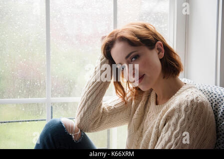 Ritratto di sorridente donna caucasica vicino alla finestra di pioggia Foto Stock