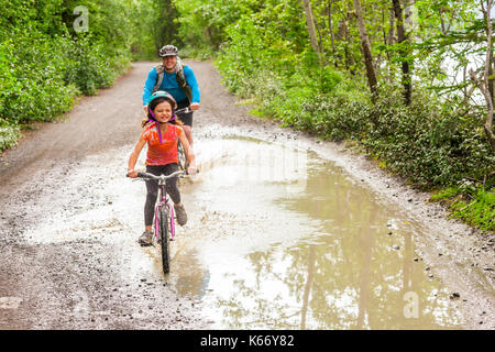 Padre e figlia di andare in bicicletta attraverso la pozza Foto Stock