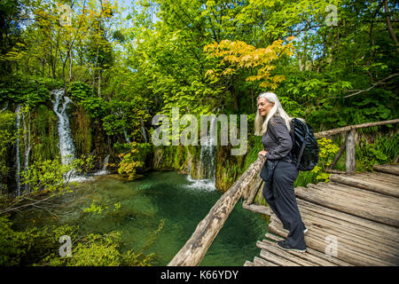 I vecchi donna caucasica sul ponte di legno ammirando le cascate Foto Stock