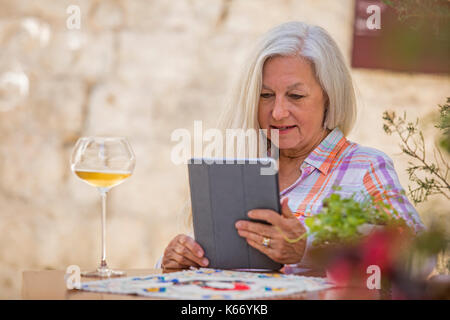 I vecchi donna caucasica bere il vino bianco e con tavoletta digitale Foto Stock