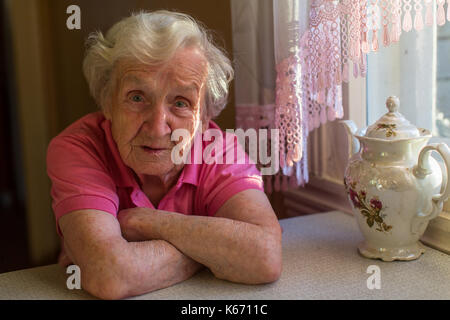 Una donna anziana con ansia si siede al tavolo della cucina. Foto Stock