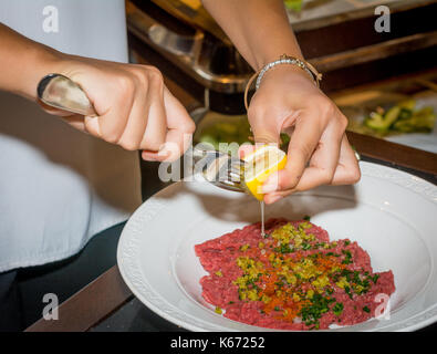 Lo chef femmina preparazione bistecca alla tartara in cucina con una speciale e salsa di limone in ristorant Foto Stock