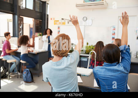 Gli alunni alzando le mani in una scuola di lezione di scienze Foto Stock