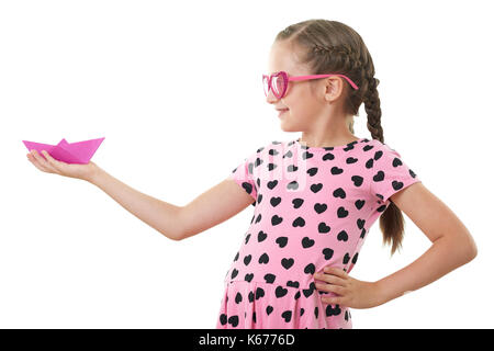 Graziosa bambina con la carta nave ritratto in studio, vestita in rosa con cuore forme, sfondo bianco Foto Stock