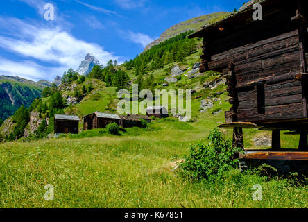 Il Cervino, Monte Cervino, con nubi intorno al vertice, dietro una montagna verde pendio con alcuni vecchi fienili Foto Stock