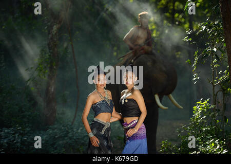 Due donne in tailandese tradizionale abbigliamento con un mahout cavalcare un elefante, Thailandia Foto Stock