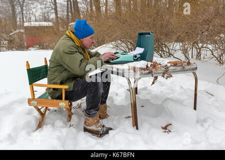 Uno scrittore seduti ad un tavolo esterno durante una tempesta di neve e digitando su una macchina da scrivere. Foto Stock