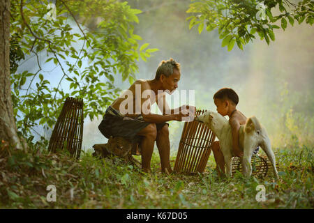 Nonno e nipote seduta nella foresta a giocare con un cane, Thailandia Foto Stock