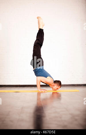 Un giovane uomo forte facendo esercizi yoga - salamba sirsasana, handstand con padmasana gambe. Foto Stock