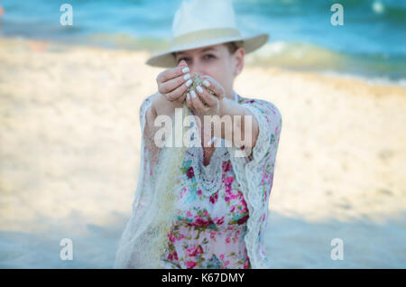 Donna in piedi sulla spiaggia con sabbia che corre attraverso le mani Foto Stock