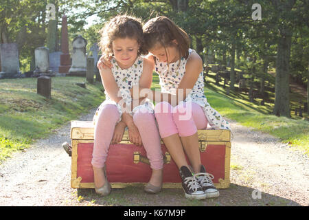 Due bambine a sedersi su una valigia in un cimitero, gridando con le braccia intorno a ciascun altro Foto Stock