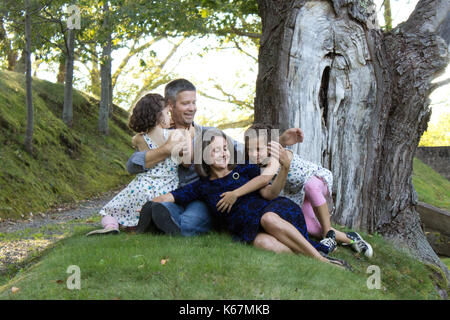 I genitori avvolgono i loro due figlie fino in una vacanza estiva abbraccio sotto un albero Foto Stock