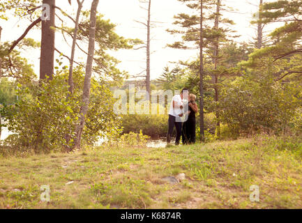 Un ampio riprese di un uomo e di una donna tenendo i loro cani in estate il sole da un lago Foto Stock