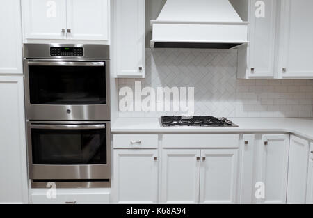 Una cucina bianca con parete in acciaio inossidabile forni, un fornello a gas e una gamma cofano. Foto Stock
