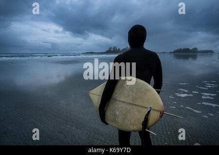 Surfer voce nell'oceano durante un inverno NUVOLOSO TRAMONTO. La foto è stata scattata in chesterman beach, Tofino, isola di Vancouver, BC, Canada. Foto Stock